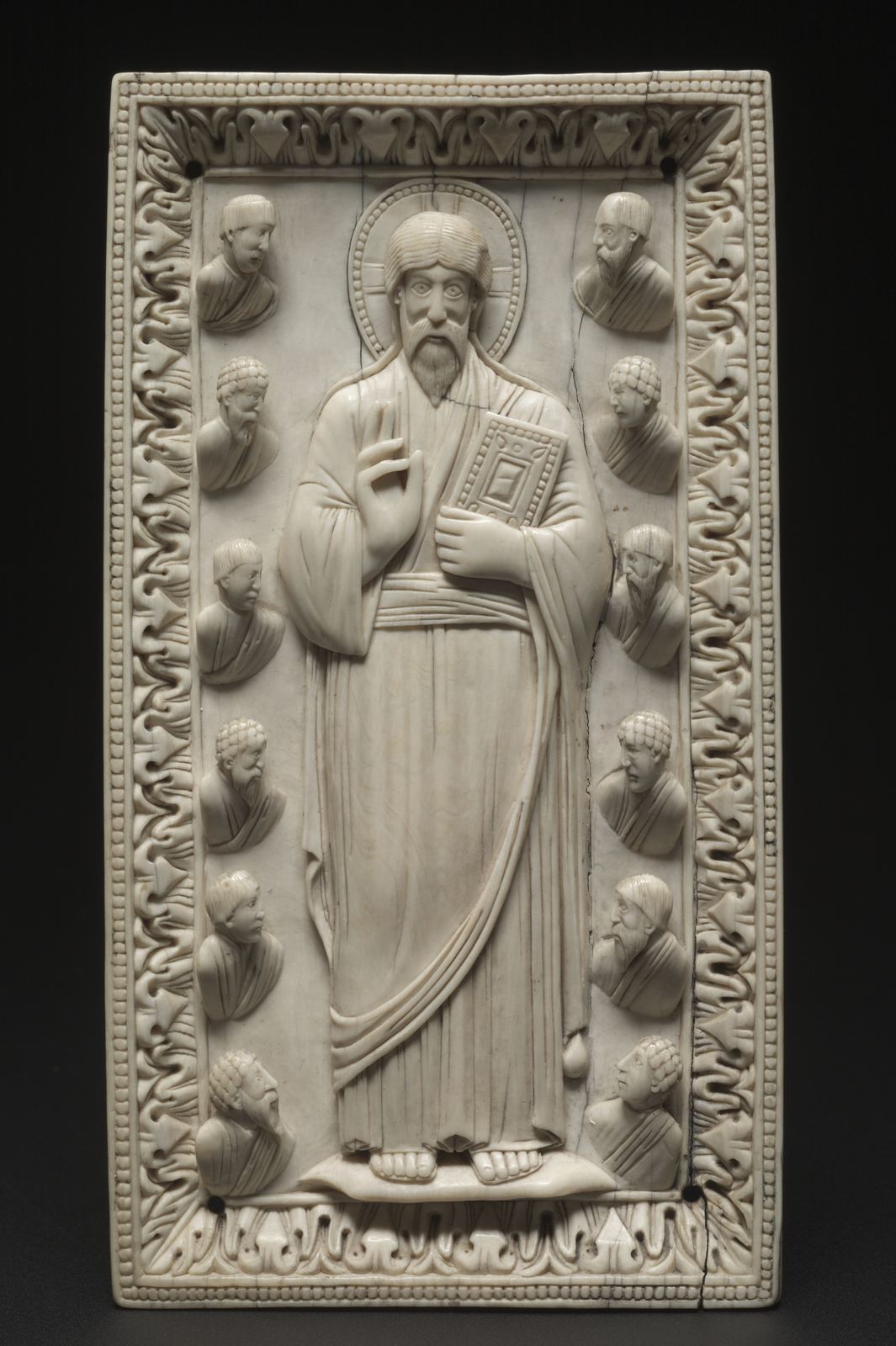 Placa de marfim esculpida: Cristo de pé ao centro, com um livro na mão esquerda e a direita erguida, ladeado por doze bustos de apóstolos em duas colunas.